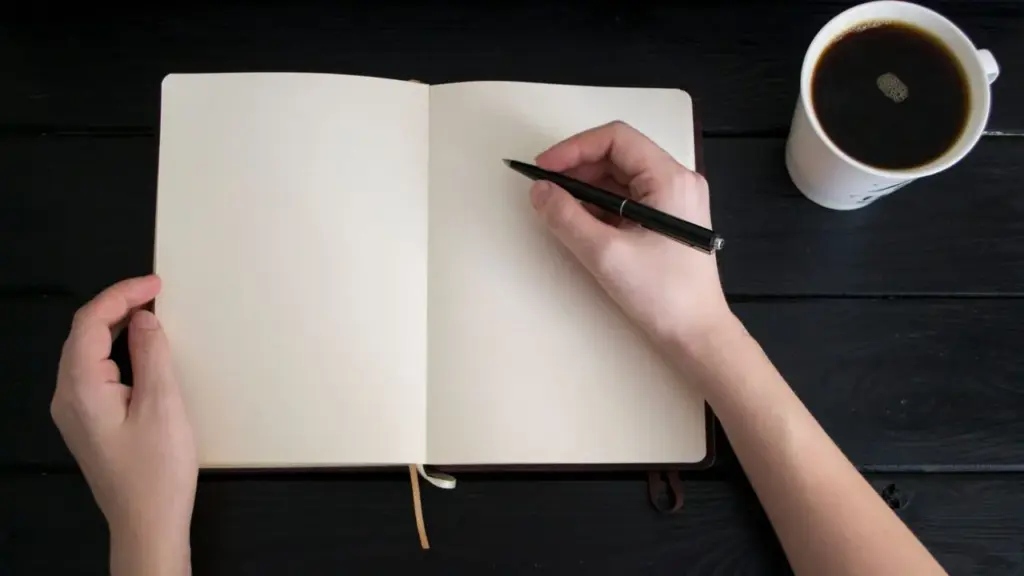 Hände schreiben in ein Notizbuch neben einer Kaffeetasse